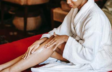 women in white robe moisturising her legs